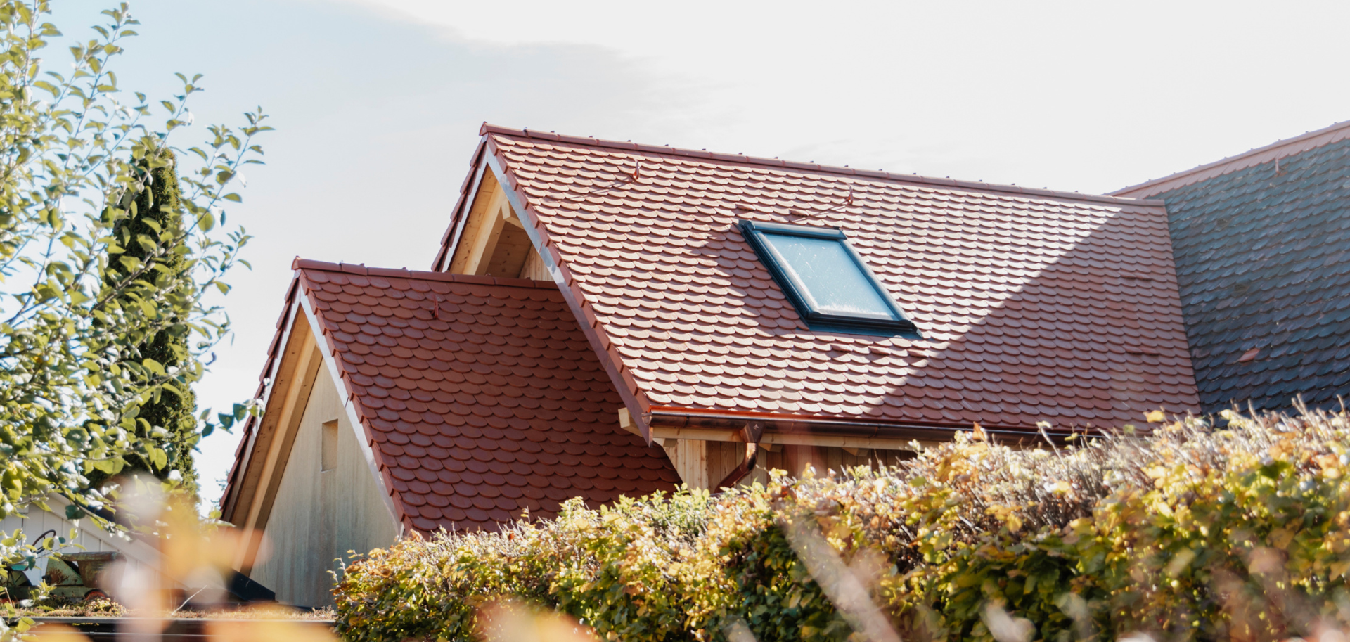 Ein aufgestocktes und mit Biberschwanzziegel gedecktes Dach der Zimmerei Huber, Anischt des Dachs über die Hecke.